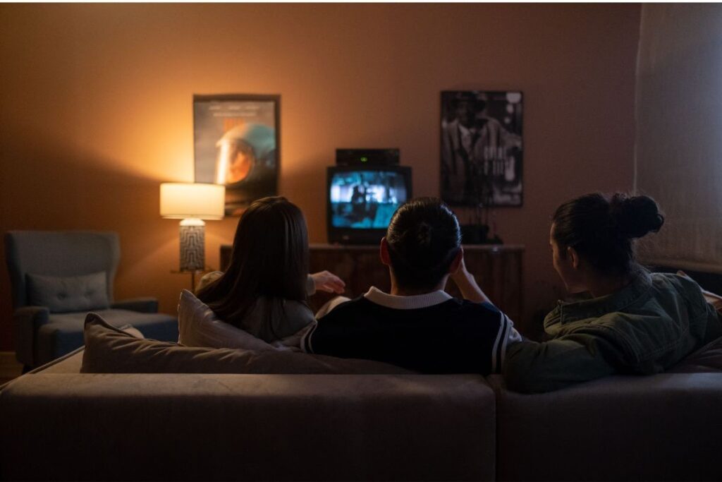 Family sitting together on a sofa watching television in a warmly lit living room during the evening.